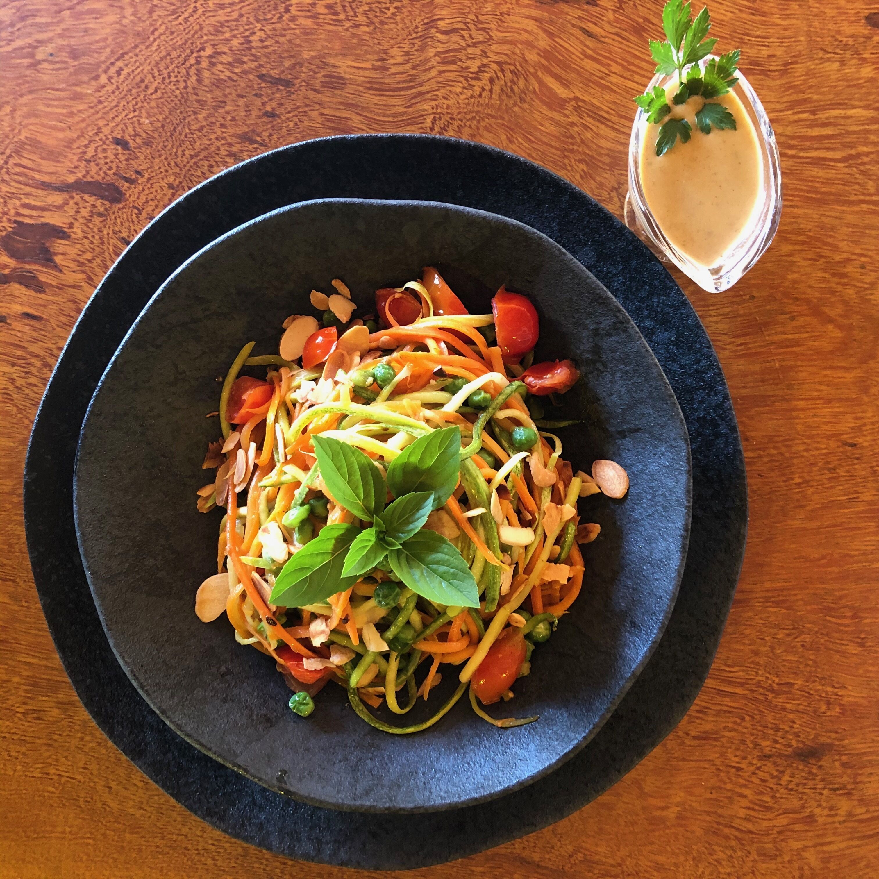 A bowl of salad with various vegetables and a glass of a creamy beverage on a wooden table.