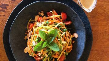 A bowl of salad with various vegetables and a glass of a creamy beverage on a wooden table.