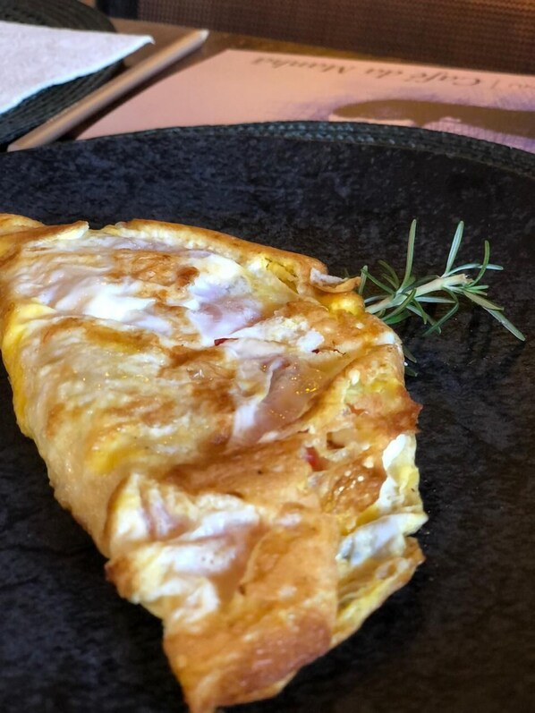 A folded omelette on a black plate with a sprig of rosemary. - CANTO DO IRERÊ - Boutique Hotel (Atibaia)