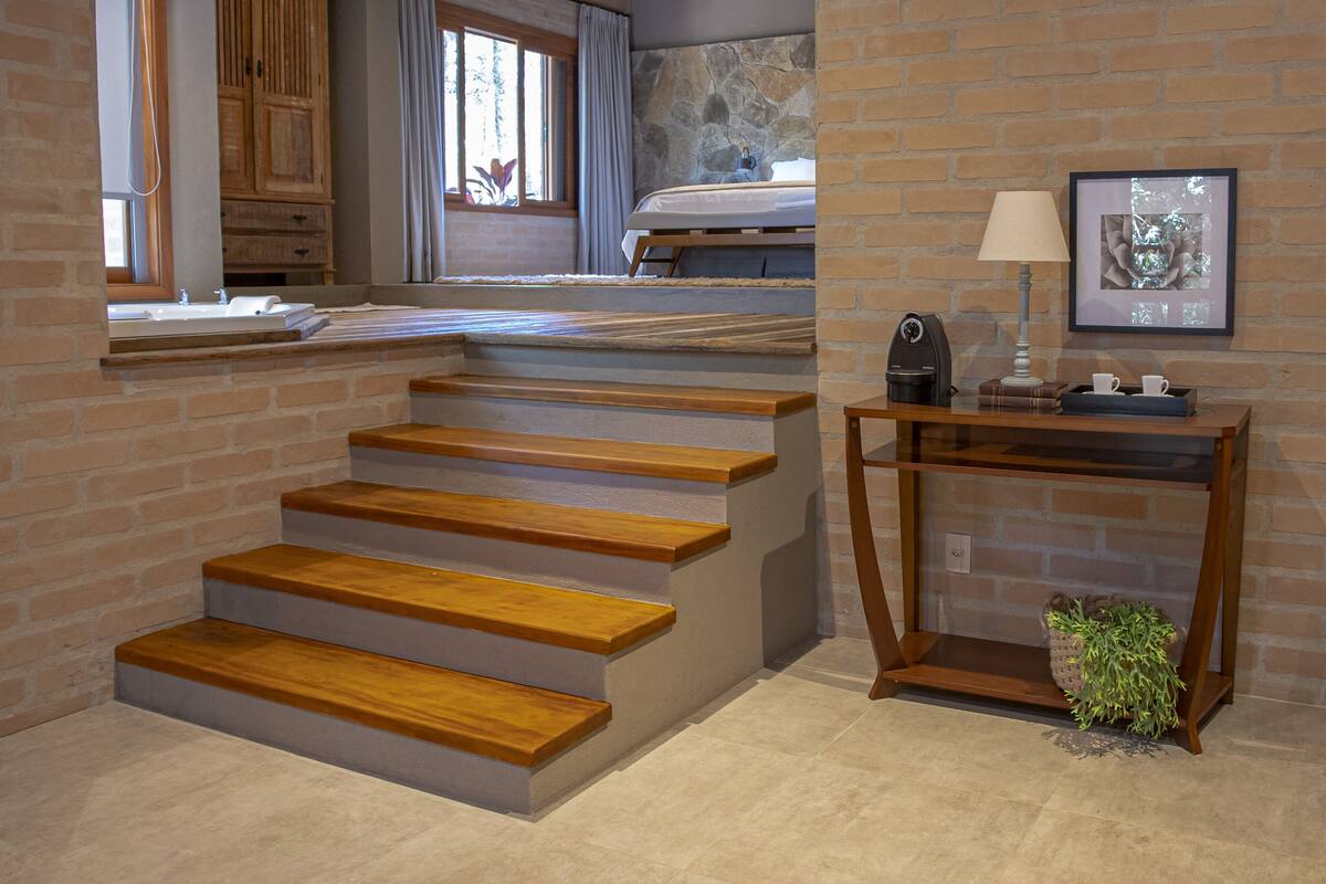 Una escalera con escalones de madera que lleva a un dormitorio con pared de piedra y un cuadro enmarcado.