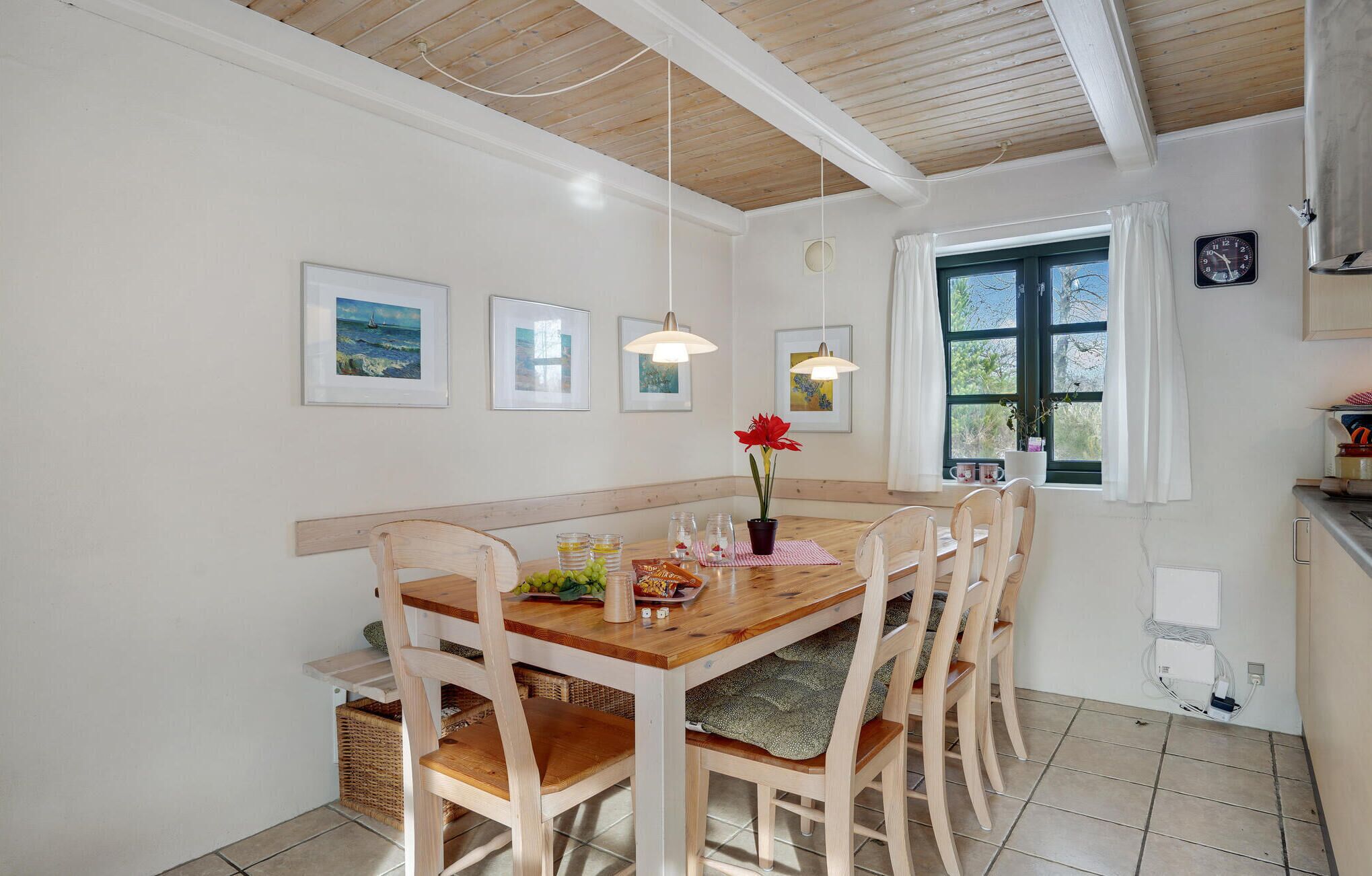 A dining area with a wooden table and chairs, framed artwork on the walls, and a window with curtains.