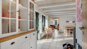 Eine geräumige Küche mit weißen Schränken, ein Essbereich mit Holzsesseln und ein Blick ins Freie durch große Fenster.