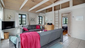 Ein gemütliches Wohnzimmer mit grauem Sofa, einem Fernseher und einem Essbereich mit Tisch und Stühlen.