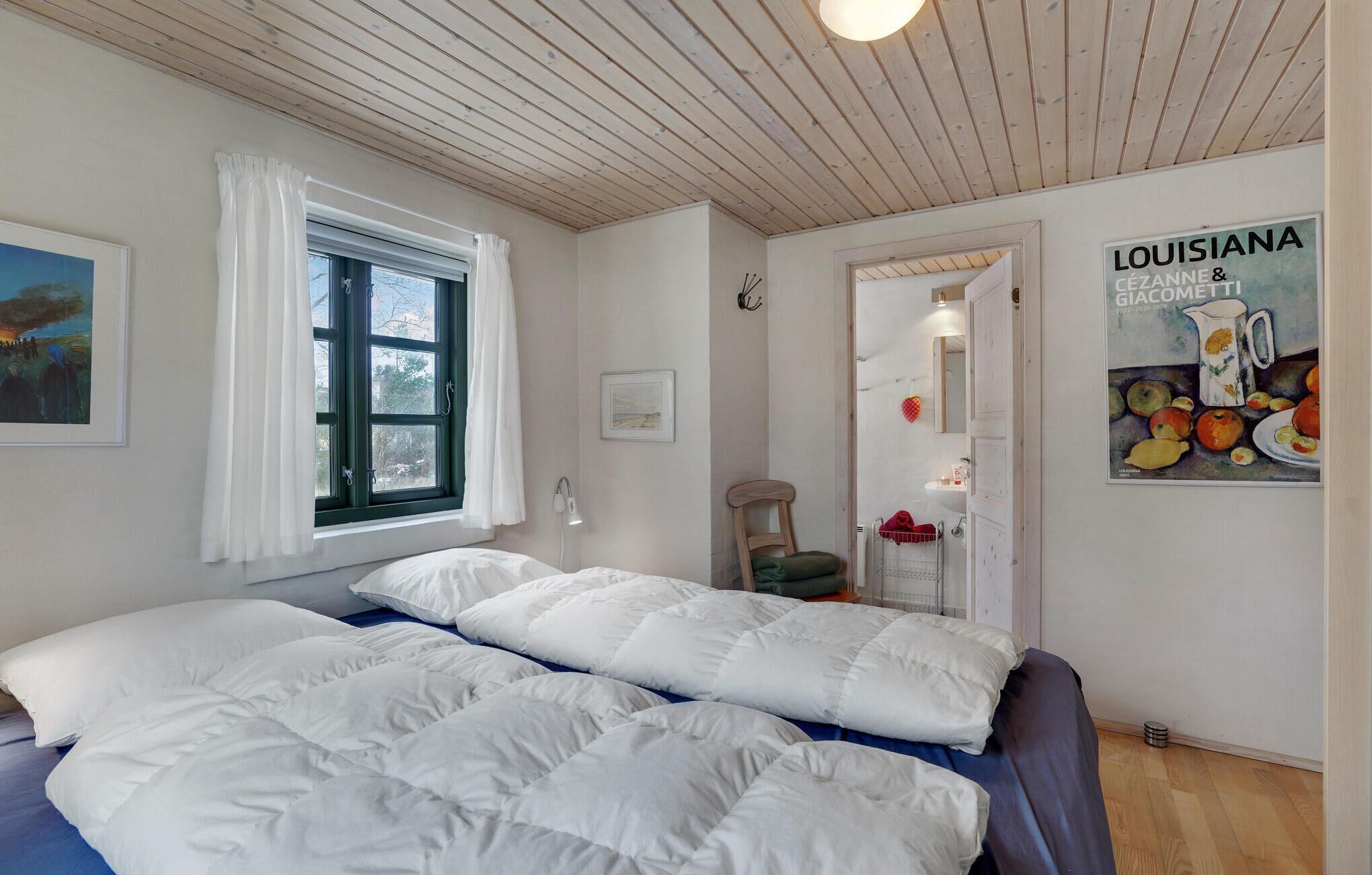Une chambre à coucher avec un lit, une fenêtre avec des rideaux, un tableau et une affiche accrochée au mur.