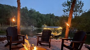 Une terrasse au bord du lac, avec un foyer, des fauteuils Adirondack et un quai doté d’un petit chalet.