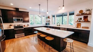 Une cuisine moderne avec des meubles de couleur sombre, un grand îlot central doté de tabourets, un four à micro-ondes et un four traditionnel.