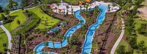 Vue aérienne d’un complexe hôtelier avec une piscine sinueuse, des palmiers et une plage.