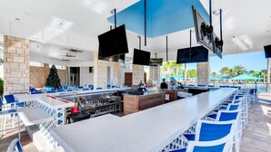 Een buitengebied met een bar, een lange toonbank, blauw-witte zitplaatsen en een stenen achtergrondmuur.