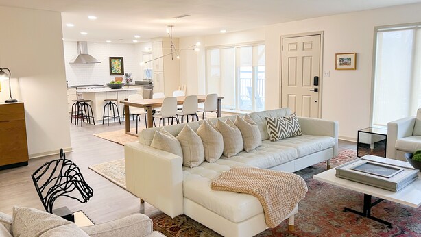 A modern living room with a white sofa, a coffee table, and a dining area with a white table and chairs.