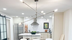 A modern kitchen with white cabinets, a wooden dining table, and a large island with a bowl of fruit.