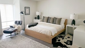 A modern bedroom with a large bed, bedside tables, a floor lamp, a chair, and a rug.