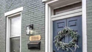 A gray brick house with a blue door, a wreath, and a welcome mat.