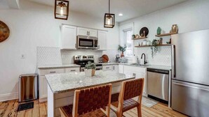 A modern kitchen with white cabinets, a central island, stainless steel appliances, and wooden flooring.