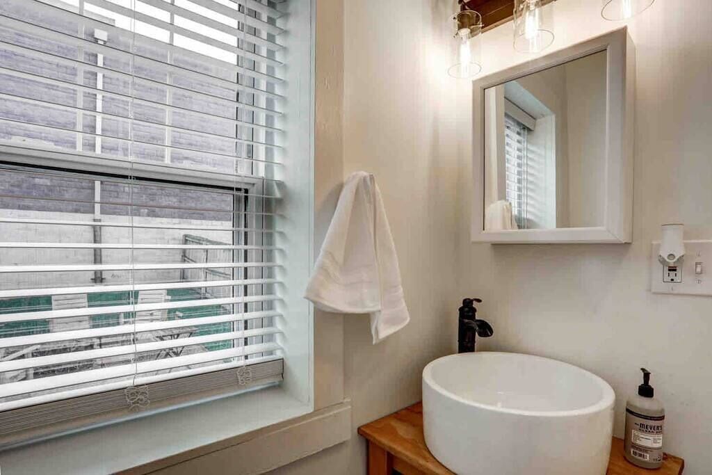 Une salle de bain avec une grande fenêtre, un lavabo, un miroir et une serviette accrochée au mur.