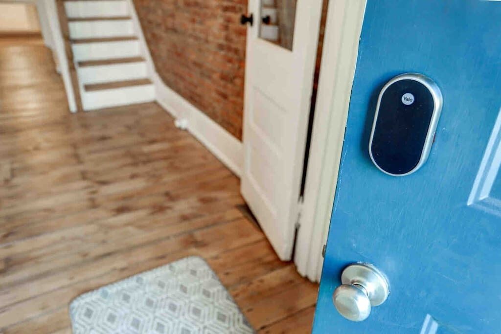 Una puerta azul con cerradura Yale, suelo de madera y alfombra blanca con diseño.