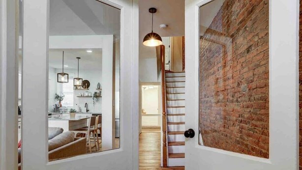A hallway with a wooden floor, a brick wall, and a staircase leading to another room.