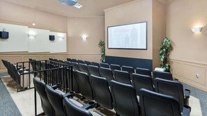 Un salón de conferencias con filas de sillas negras, una pantalla de proyector y una pizarra.