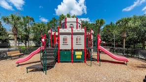 Un parque infantil con una estructura que parece un castillo, toboganes y un área vallada con bancos.
