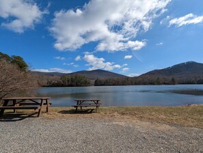 Zona de grava amb dues taules de picnic de fusta i una vista despejada d'un llac envoltat de turons.