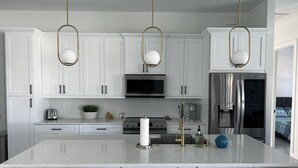 A modern kitchen with white cabinets, a central island, stainless steel appliances, and pendant lighting. - New 4bd/3ba w/ private pool, fenced yard, outdoor kitchen, close to everything! (Cape Coral)