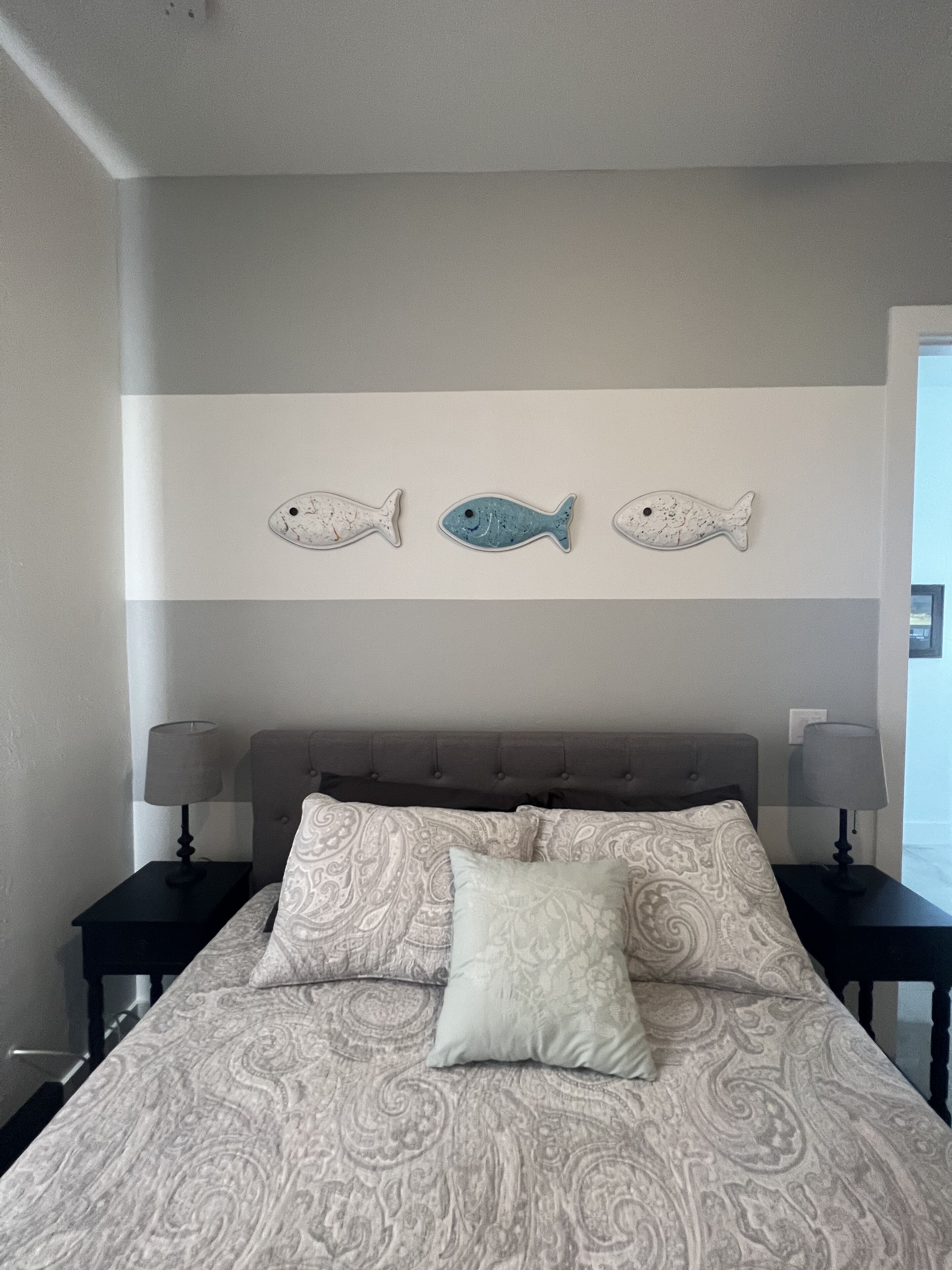 A bedroom with a bed, two nightstands, two lamps, and three wall-mounted fish decorations.