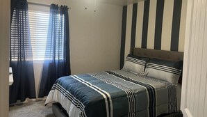 A bedroom with a bed, a ceiling fan, and a window with curtains.