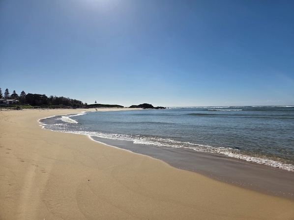 A beach with a clear sky, sandy shore, and calm sea.