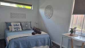A bedroom with a bed, pillows, a bedside table with a plant, and a window with a view.