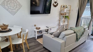A modern living room with a sofa, dining table, chairs, a TV, and a bookshelf.