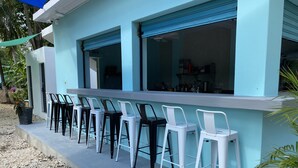 A bar area with a row of white and black bar stools, a light blue exterior, and a concrete floor. - this place will bring lots of peace to enjoy the sun and the beach! (San Antero)