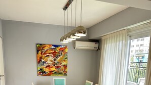 Ein Essbereich mit einem weißen Tisch und blaugrünen Stühlen, einem farbenfrohen abstrakten Gemälde an der Wand und Blick ins Grüne.