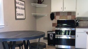 A compact kitchen with white cabinets, a black stove, and a small trash bin. - Amy's Oasis in Omaha (Omaha)