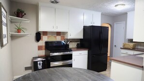 A compact kitchen with white cabinets, a black refrigerator, a stove, and a microwave. There are two potted plants on the shelves. - Amy's Oasis in Omaha (Omaha)
