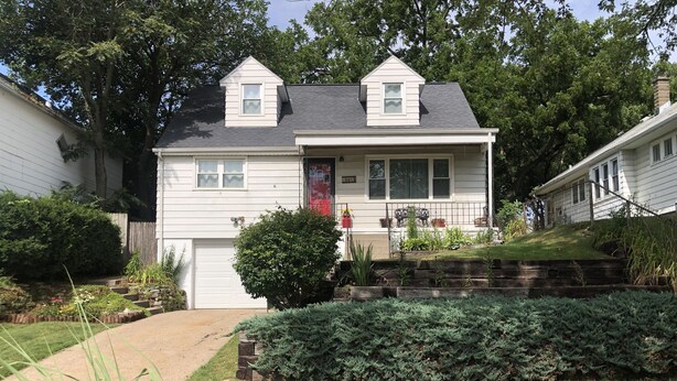 A two-story house with a front porch, a garage, and a well-maintained garden with various plants and shrubs. - Amy's Oasis in Omaha (Omaha)