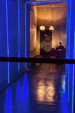 A modern interior with a reflective floor, blue lighting, and a person speaking at a podium. - Nido Sky (Medellín)