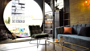Una sala de estar moderna con un ventanal circular grande, un sillón verde, un sofá azul y una mesa de centro de vidrio.
