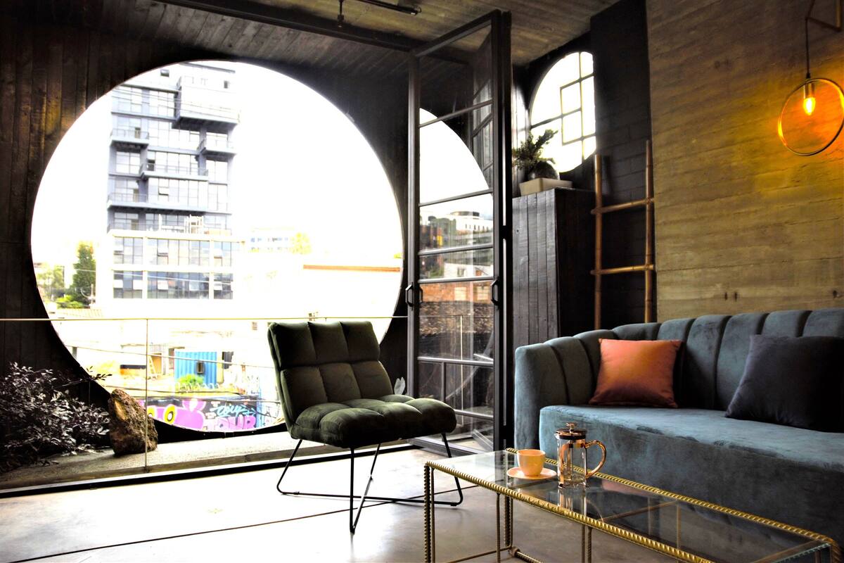 A modern living room with a large circular window, a green armchair, a blue sofa, and a glass coffee table.