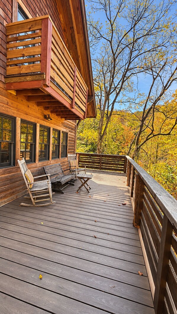 A wooden deck with a bench and a table, overlooking a forested area.