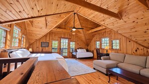 A cozy, wooden cabin interior with a loft bedroom, a sofa, and a dining table.