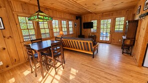 A wooden interior with a dining table, chairs, a sofa, a television, and a fireplace.