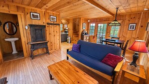 A wooden cabin interior with a sofa, a table, a lamp, and a fireplace.