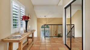 Un pasillo con un banco de madera, un jarrón con flores y vistas a un balcón con barandilla.