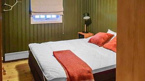 Ein Schlafzimmer mit einem Bett, einem Nachttisch mit Lampe, einem Fenster mit Jalousien und einer Wandleuchte.