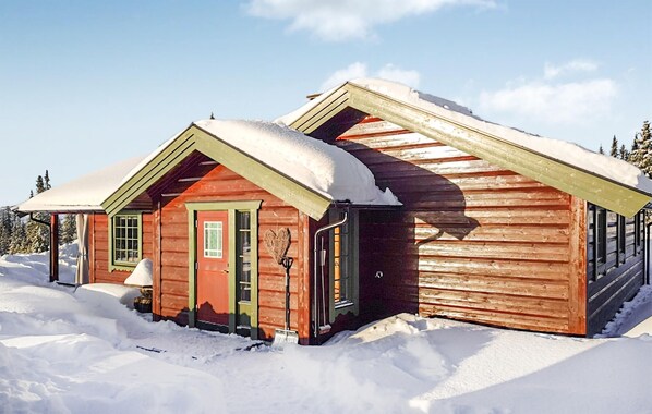 Una cabaña de madera con techo nevado y un pequeño porche.