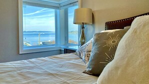 A bedroom with a bed, a lamp, and a view of the ocean through a window. - Luxurious Penthouse with Bay View in Old Town Tacoma (Tacoma)