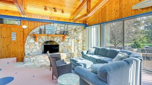A cozy room with a stone fireplace, wooden ceiling, and a large window offering a view of the outdoors.