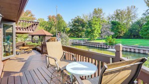A wooden deck with outdoor seating, a small table, and a view of a water body and greenery.