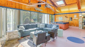 A wooden interior with a sectional sofa, wicker chairs, a small table, and a hot tub.