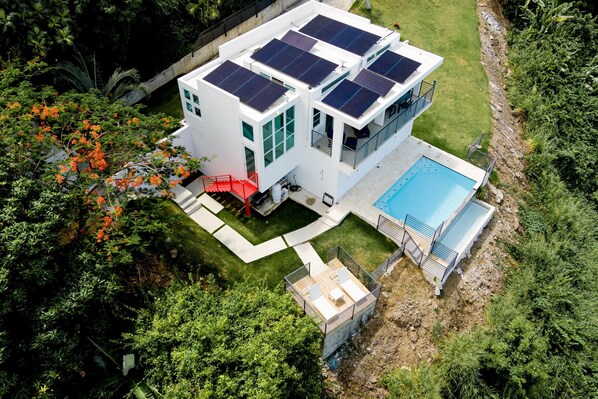 Una casa moderna con piscina, paneles solares y una escalera roja.