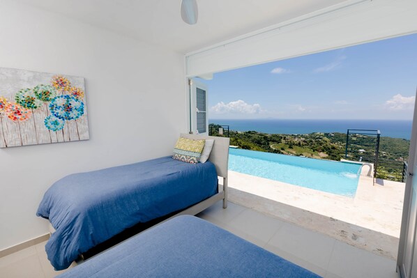 A bedroom with two beds, a painting, and a view of a swimming pool and landscape.